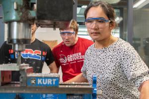 Female student working on machine wearing safety glasses, in machine shop